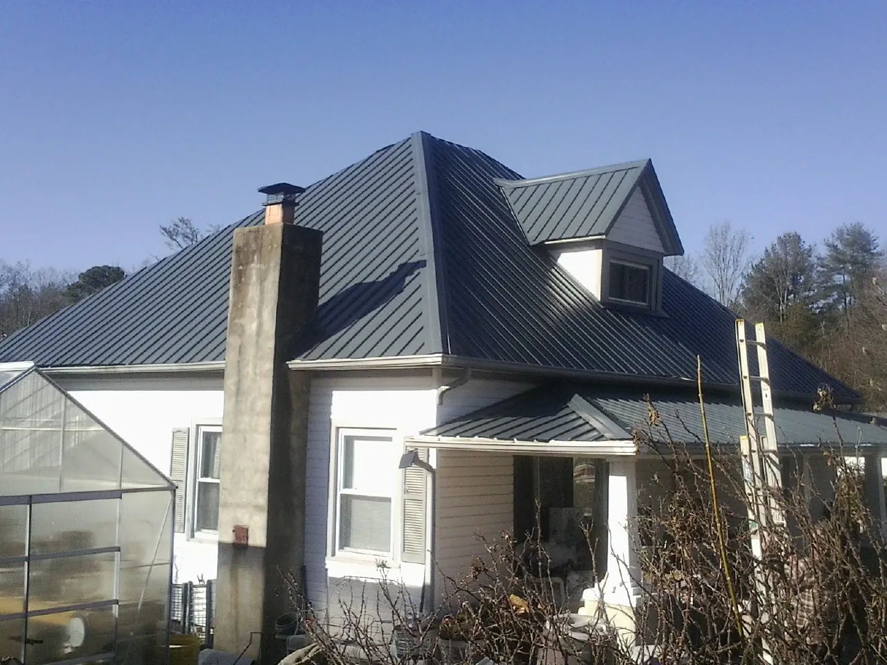 Dark blue standing seam metal roof on a white farmhouse with dormer — Slate & Tile Roof Repair by Roofing Brothers in Oriskany