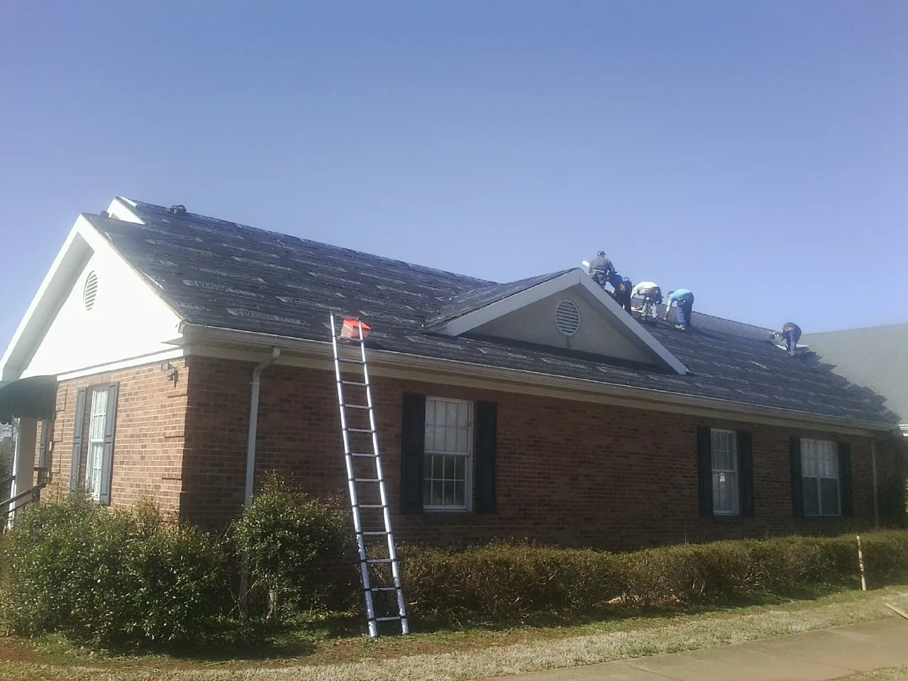 Crew tearing shingles off a brick ranch roof with a ladder set — Emergency Roof Repair work by our crew in Oriskany