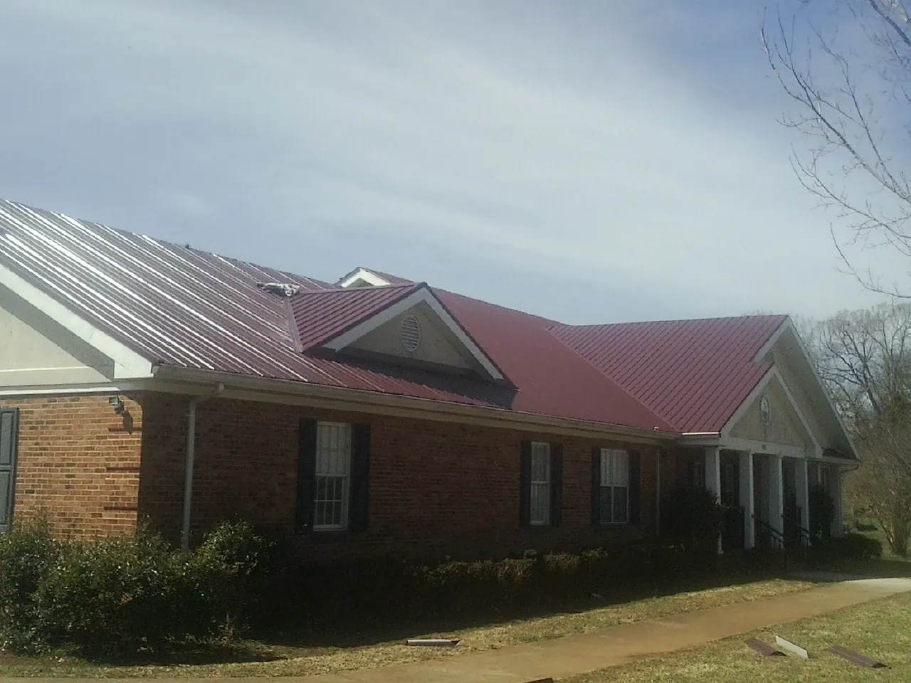 Red metal roof with gabled entries on a long brick building, from a Hail Damage Roof Repair job in Oriskany