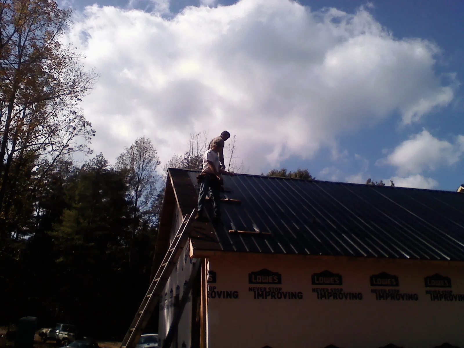 Roofer fastening dark metal panels high against a cloudy sky, from a Roof Inspection job in Oriskany