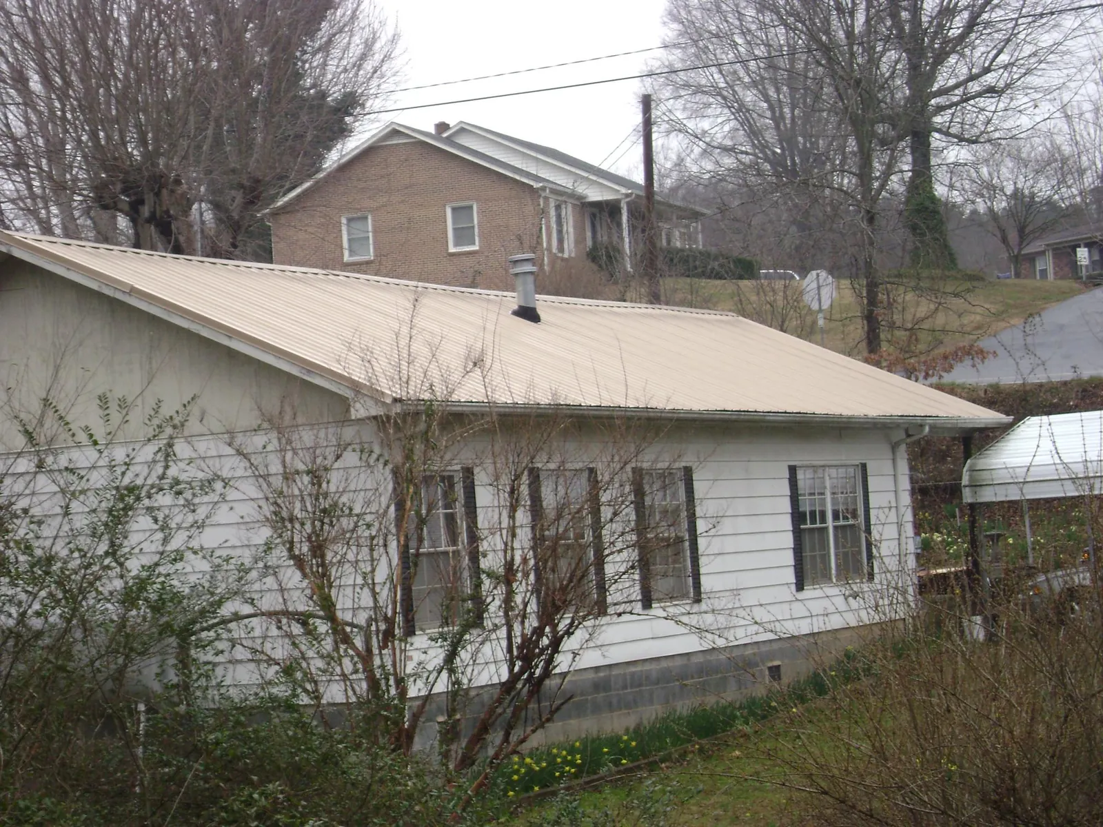 Tan metal roof on a white sided house set into a hillside — Commercial Roofing by Roofing Brothers in Oriskany