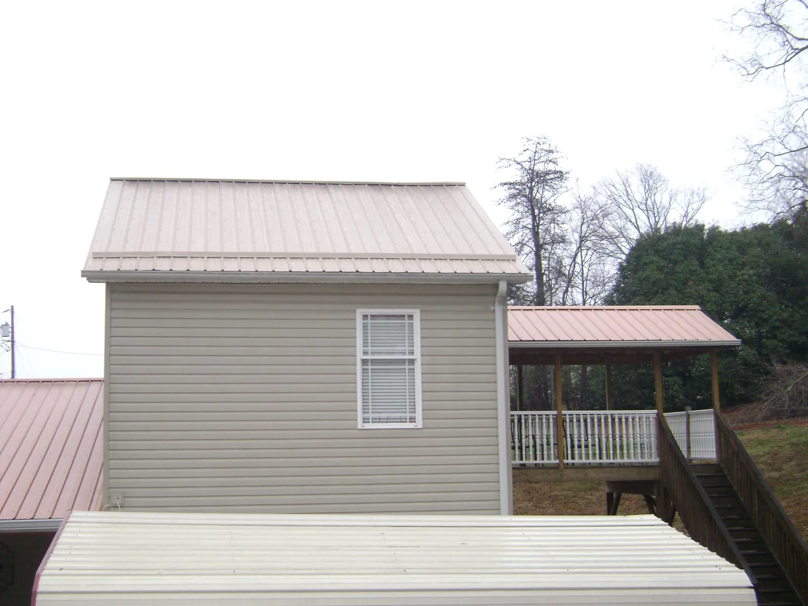 Tan metal roofs on a two story addition and attached porch, from a Roof Replacement job in Oriskany